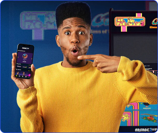 Man holding and pointing at an iphone with arcade games in the background